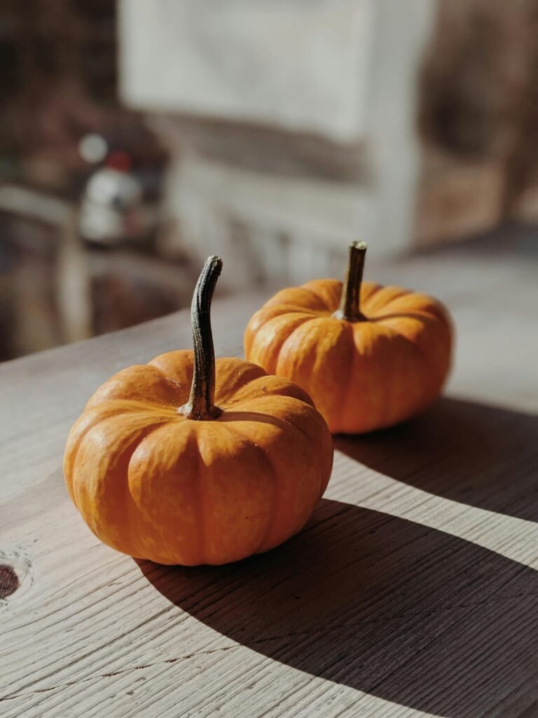 Close-up of two orange pumpkins on a wooden surface with sunlight casting shadows, ideal for autumn themes.